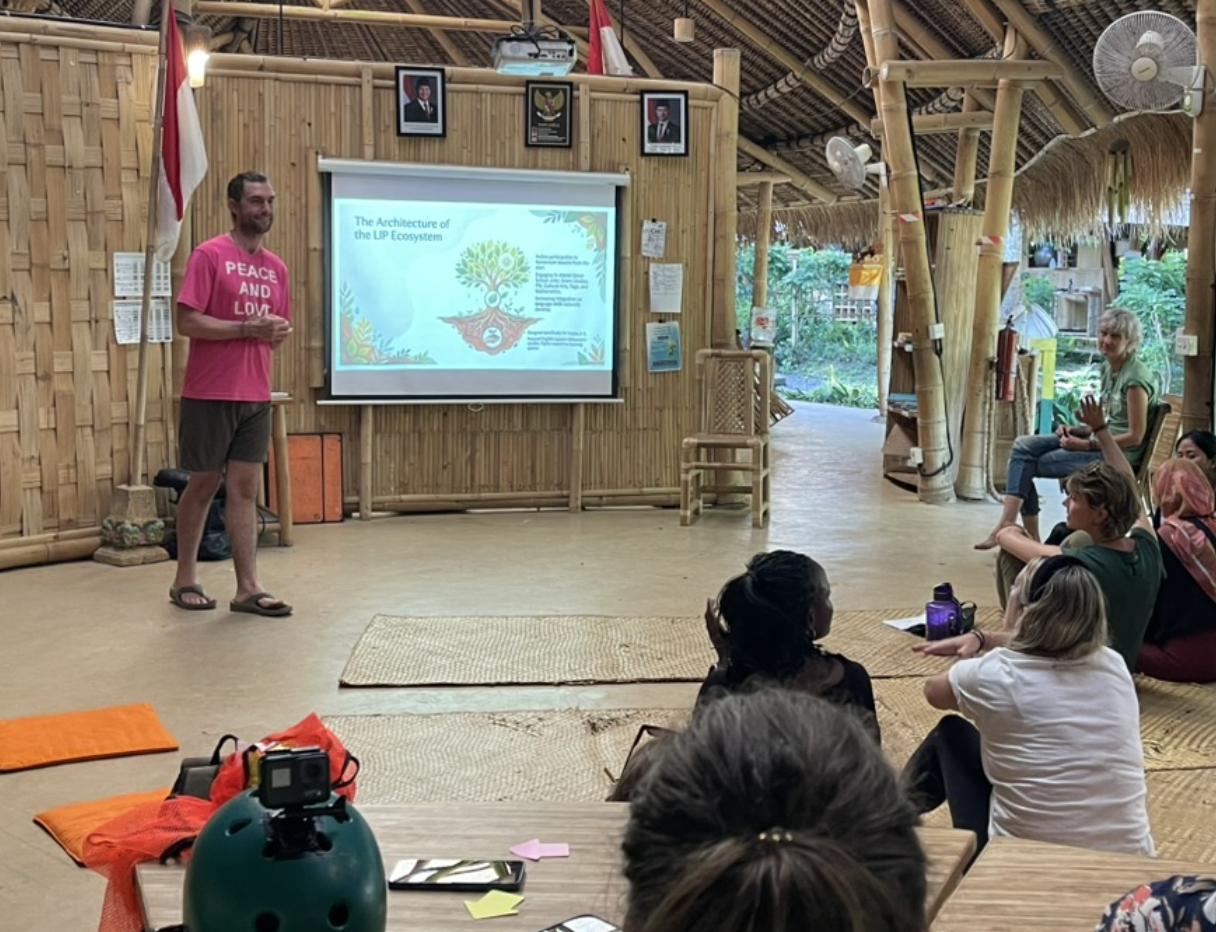 Man presenting to seated audience in bamboo pavilion
