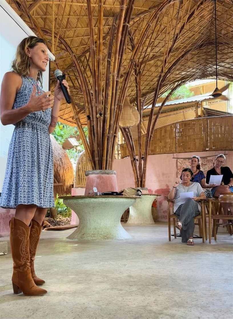 Woman speaking to seated audience in bamboo pavilion
